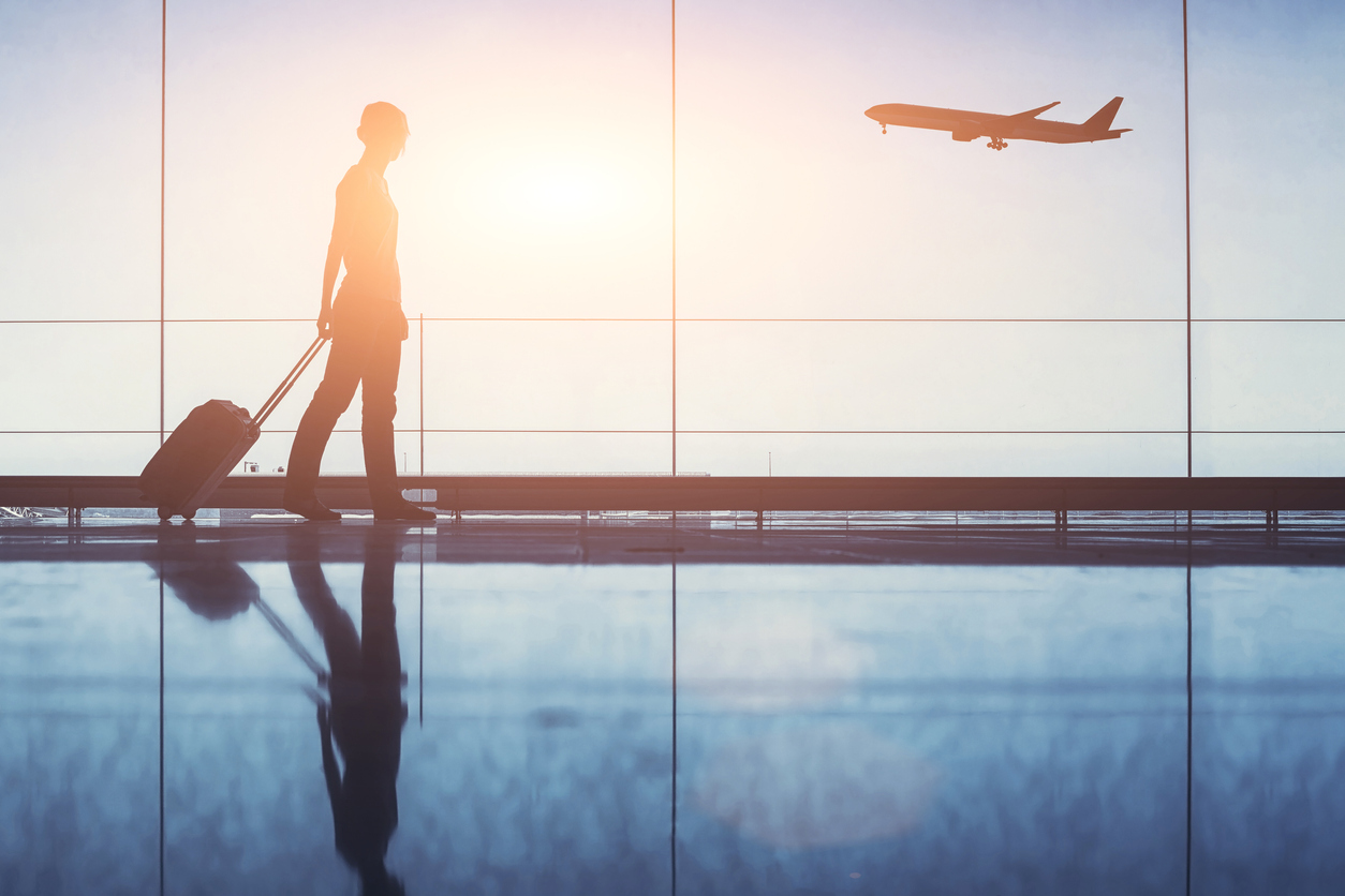 A traveler pulls their luggage behind them while an airplane takes off in the background.